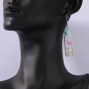 Close-up detail of a cute glass drifting bottle earring featuring a pink dry flower and glitter inside.