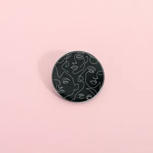 Dettaglio della spilla rotonda in metallo con design di viso astratto in stile linea minimalista.