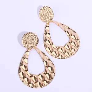 Vue détaillée de boucles d'oreilles dorées élégantes au design texturé et géométrique.
