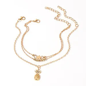 Meerlaagse goudkleurige enkelband met ananas hanger en delicate kettingdetails strand.