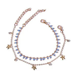 Dubbellaagse gouden metalen enkelband met blauwe kraaltjes en bedels, detailweergave.
