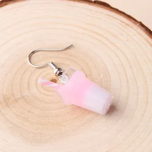 Close-up detail of cute pink boba drink cup shape drop earring on a rustic wood slice.