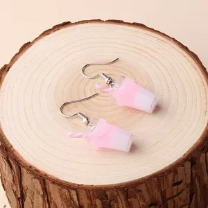 Close-up detail of cute pink and white bubble tea cup shaped dangle earrings on wooden slice.