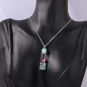 Close up view of a clear glass wishing bottle pendant necklace with pink flower and glitter.