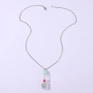 Clear glass wishing bottle pendant necklace featuring a dried pink flower and silver chain.