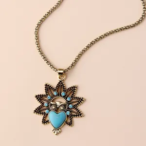 Close-up of vintage gold owl pendant necklace with blue crystals and heart stone detail.