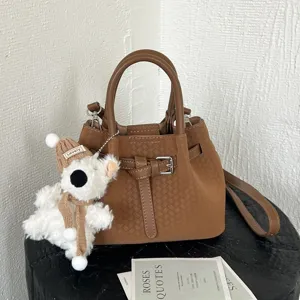 Bolso cubo marrón trenzado de moda para mujer con adorable colgante de oso y correa.