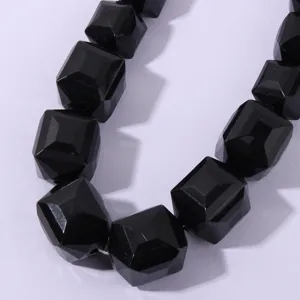 Primo piano dettaglio di collana con perle geometriche sfaccettate nere, minimalista.