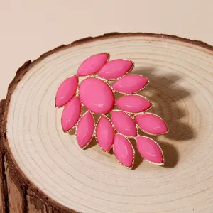 Detail shot of a statement pink acrylic rhinestone cluster brooch with gold trim on wooden slice.