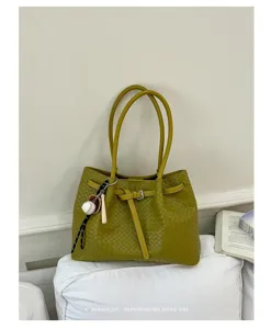 Detailed view of yellow-green woven leather tote bag with baseball charm and belt accent.