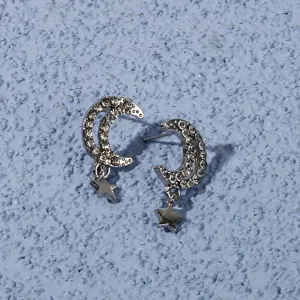 Detailed close-up of silver-tone rhinestone crescent moon and dangling star stud earrings.