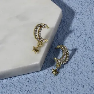 Detailed shot of trendy rhinestone moon and star drop earrings in gleaming gold tone design.
