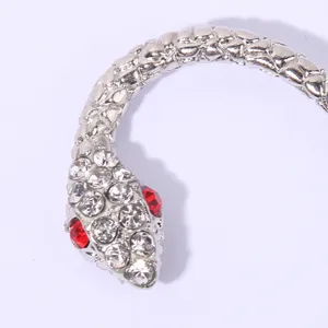 Close-up of sparkling rhinestone snake ear cuff with red eyes, showing textured metal scales.