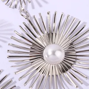 Close-up detail of silver starburst pendant with central white pearl, elegant metallic design.