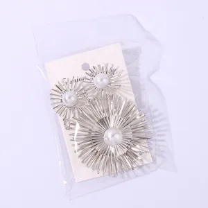 Detail shot of metallic sunburst star earrings with central faux pearl, elegant long design.