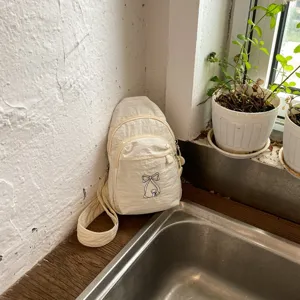 Λεπτομερής όψη γυναικείας τσάντας στήθους με κέντημα φιόγκου, ανοιχτό μπεζ τσαντάκι.