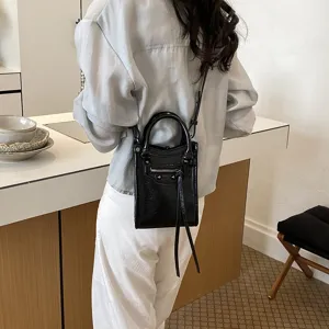 Black leather-look mini crossbody tote bag with top handles, chic studded front zip pocket.