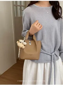 Vista dettagliata della elegante borsa a secchiello marrone con ciondolo orsetto e chiusura.