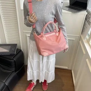 Detalle de bolso de viaje bandolera de nailon rosa con asa en un entorno de estilo de vida interior.