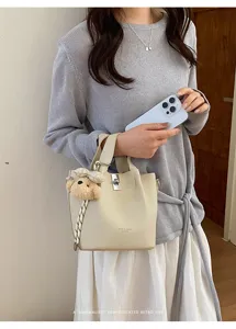 Borsa a secchiello minimalista chic in pelle beige con ciondolo orsetto e fibbia.