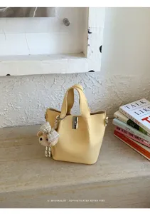 Chic borsa a secchiello in pelle giallo chiaro con chiusura a torsione in metallo e charm orsetto.