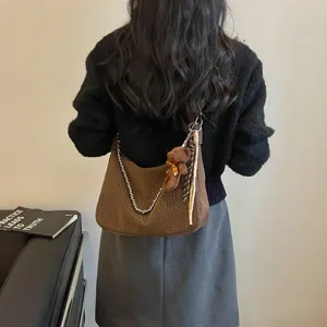 Detailansicht einer braunen geflochtenen Schultertasche mit Kettengurt und Bärenanhänger.