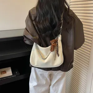 Detailansicht der stilvollen weißen Schultertasche mit Metallkette und Bärenanhänger.