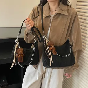 Detailaufnahme der schwarzen geflochtenen Umhängetasche mit Kette und Bärenanhänger.