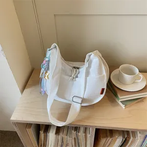 Dettaglio della borsa a tracolla bianca casual in stile hobo con ciondoli e tasca frontale.