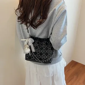 Detail shot of black quilted chain bucket bag with pearl pendant showcasing fashion style.
