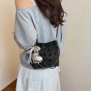 Detail view of fashionable black quilted bucket bag with pearl lace ribbon and heart charm.