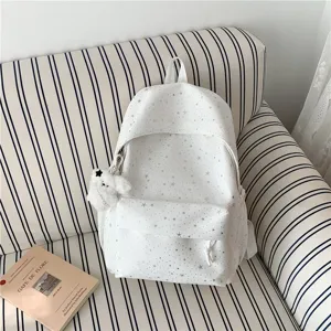 Vue détaillée du sac à dos blanc imprimé étoiles avec pendentif ours en peluche mignon canapé.