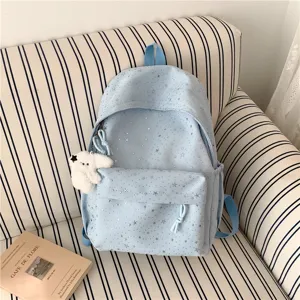 Gros plan détaillé du sac à dos bleu clair avec motif d'étoiles et charm en peluche.