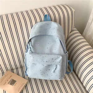Vue détaillée d'un sac à dos décontracté bleu clair avec des étoiles argentées sur canapé.