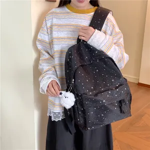 Vue détaillée du sac à dos imprimé d'étoiles porté par le modèle, montrant breloque et bretelles.