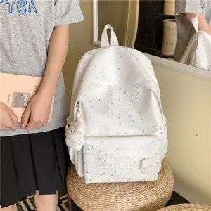 Vue détaillée du sac à dos d'école blanc à motif d'étoiles avec pendentif en peluche et poche.
