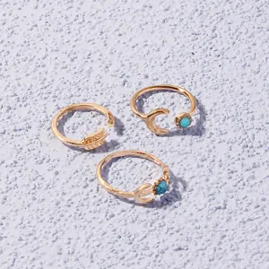 Close-up detail of three gold-tone open rings featuring turquoise stones, moon and arrow motifs.