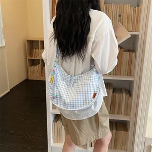 Borsa a tracolla dumpling a quadri blu e bianchi, scatto di dettaglio con libreria sullo sfondo