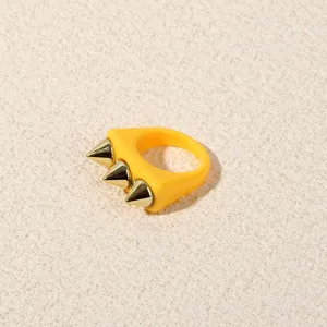 Close-up of bright yellow acrylic ring showcasing three shiny metallic gold spike studs.