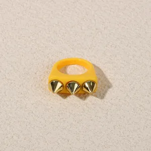 Detail shot of a yellow chunky acrylic ring featuring three gold metallic spikes for a punk style.
