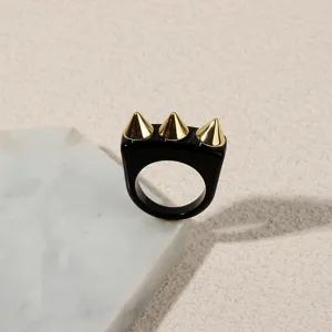 Detailed shot of black acrylic ring with gold spike studs, punk style fashion jewelry detail.