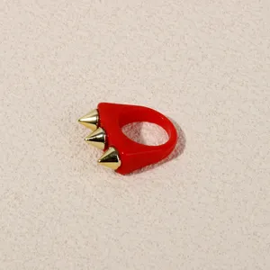 Closeup of red acrylic punk ring featuring three gold metallic spike studs for edgy style detail.