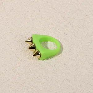 Neon green acrylic ring with three gold spike details, stylish punk style finger close up.