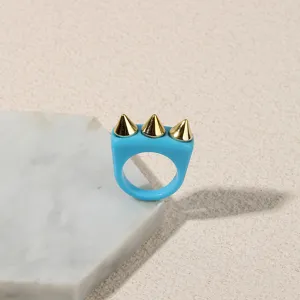 Close-up of a blue acrylic ring with three gold spike studs, punk style fashion jewelry detail.
