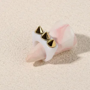 Close-up detail shot of a punk style acrylic ring featuring striking gold cone spike studs.