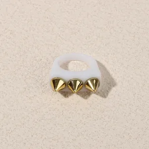 Detailed view of white acrylic ring featuring three gold tone spike rivets for edgy punk style.