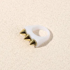 Detail close-up of white acrylic ring with gold spike studs, punk style jewelry design.