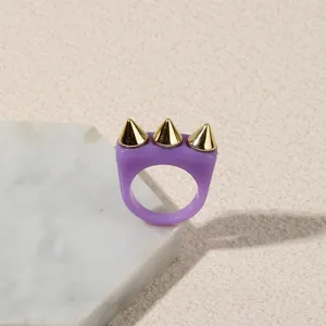 Purple acrylic ring detail with three gold spike cones on a white marble slab background.