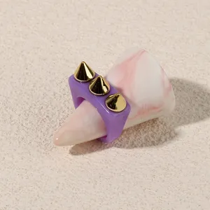 Close-up detail of a purple acrylic punk ring featuring three gold spike studs on a marble stand.