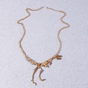 Detail shot of the gold dinosaur skeleton necklace pendant showing intricate bone links.